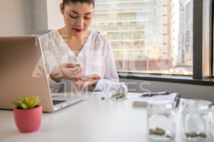 Female Cannabis Entrepreneur holding  a Bud, Working on Marketing for Marijuana Business in Bright, Soft Lit Office - The Cannabiz Agency