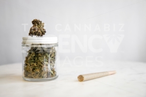 Joint and Cannabis Glass Jar on White Marble – Cannabis Dispensary Products - The Cannabiz Agency