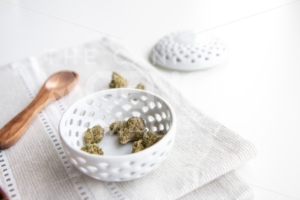 Marijuana Buds in a Porcelain Bowl on a Silver Placemat with Wooden Spoon and Lid – Minimalist Cannabis - The Cannabiz Agency