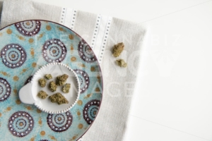 Top Down View on Marijuana Buds on a Vintage Plate atop a Silver Placemat and White Background Minimalist Cannabis - The Cannabiz Agency