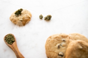 White Marble of Edible Marijuana Chocolate Chip Cookies, Cannabis Buds and Ground Weed on a Wooden Spoon - The Cannabiz Agency